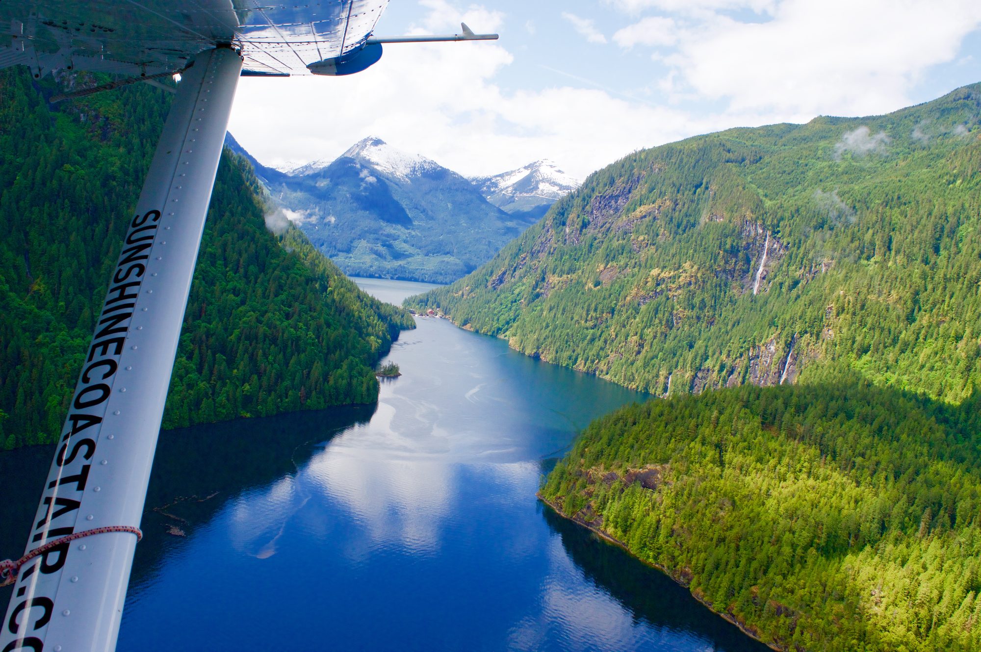 Aerial view along Princess Louisa Inlet from a floatplane, with snow-capped peaks at the head.